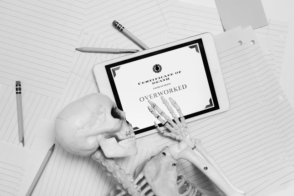 Black and white image of skeleton hand holding tablet with 'Certificate of Death' showing overworked.